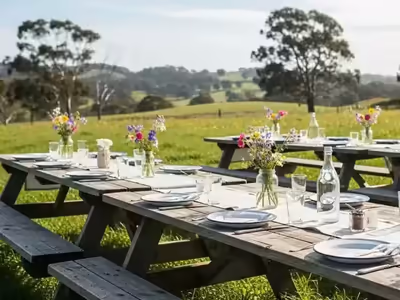 Mesa picnic de madera montada con servicio y flores en un campo