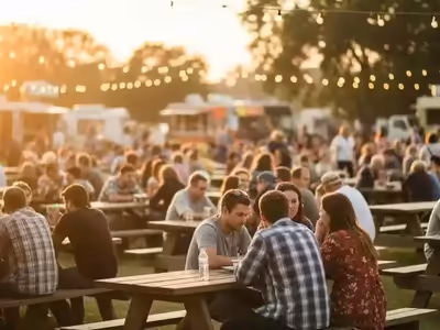 Mesas picnic llenas de gente en un evento con food trucks