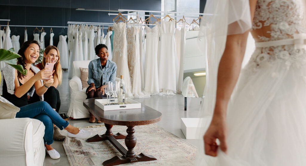 Grupo de tres personas sentadas en una tienda de ropa mirando a una persona con un vestido de novia